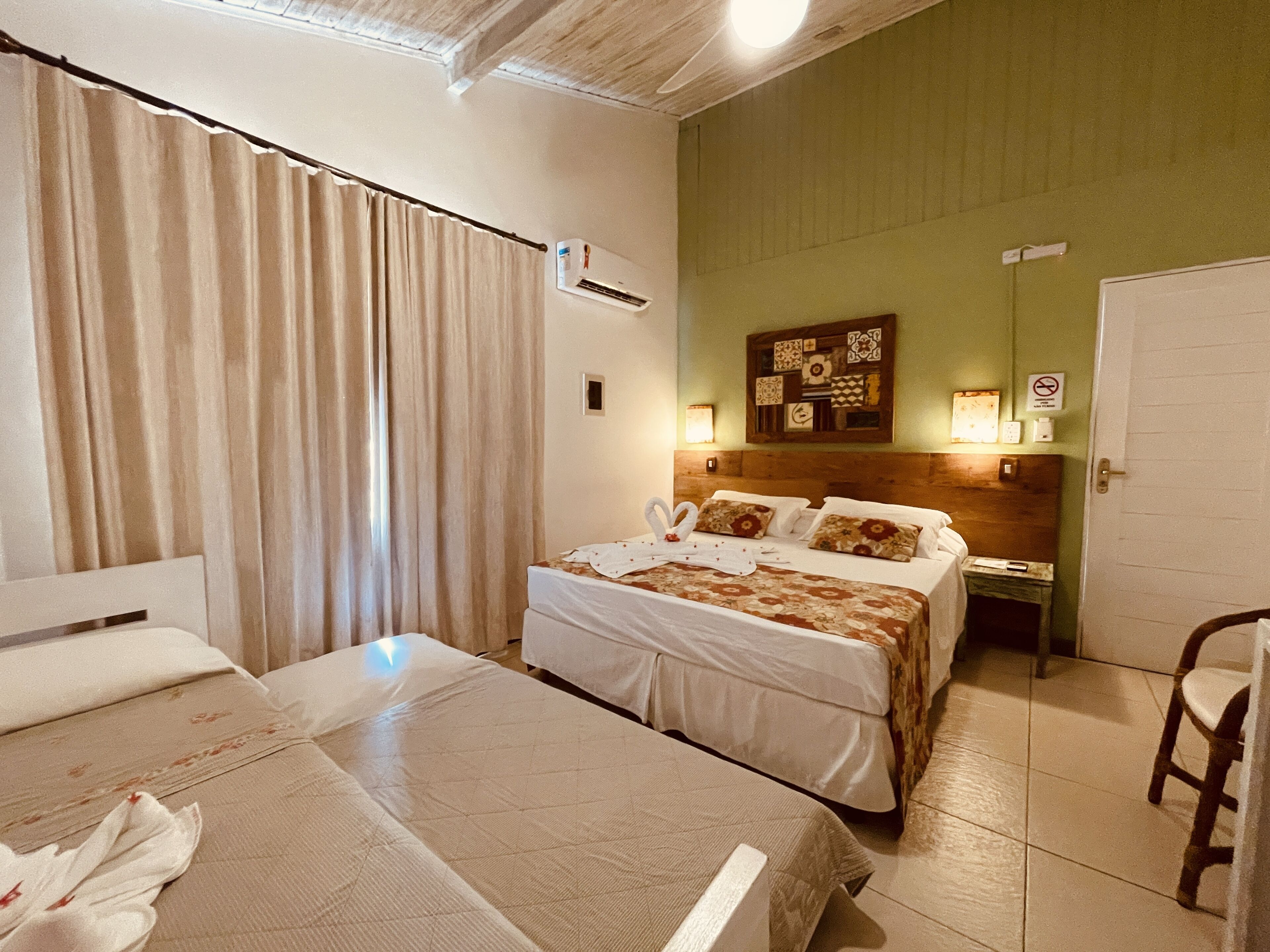 Camera d'albergo con due letti, una testiera in legno, un condizionatore d'aria a parete e una porta con il cartello 'no smoking'.