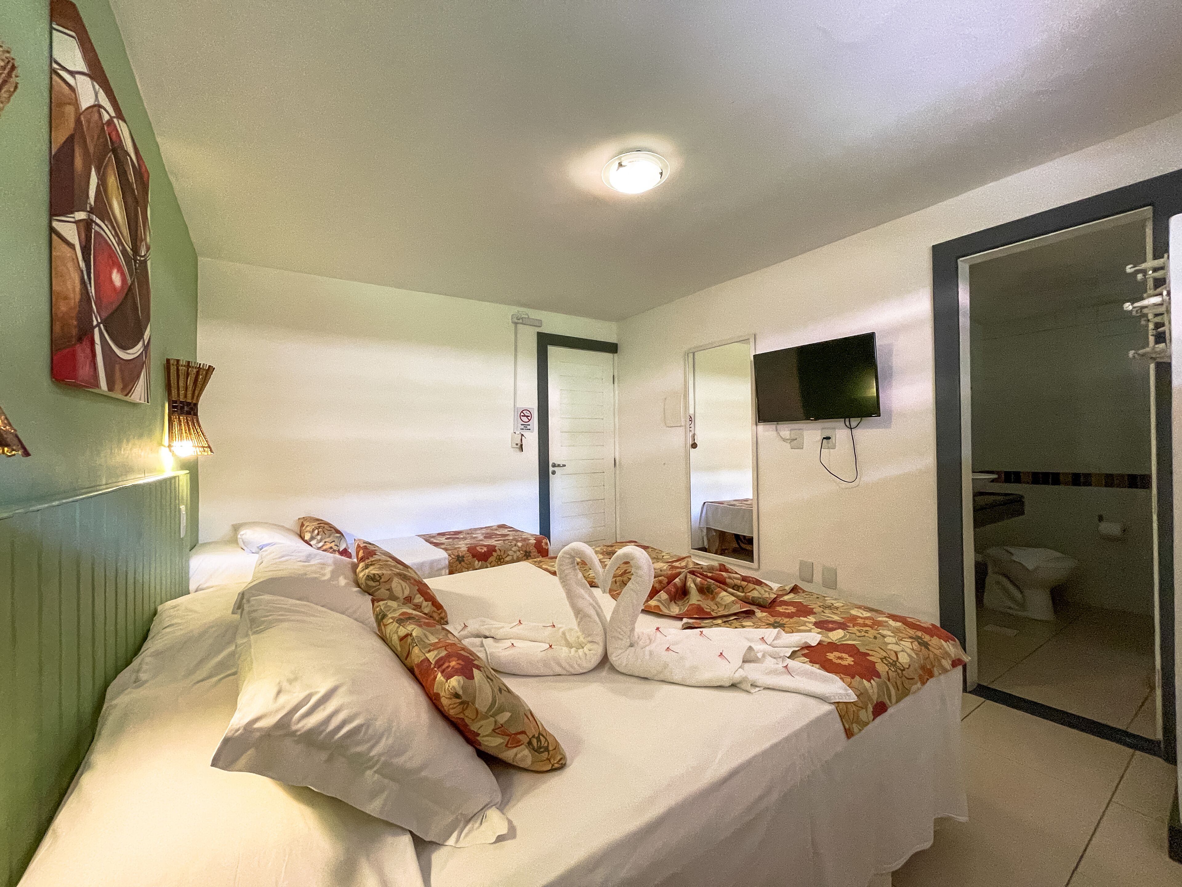 A hotel room with a bed, a television, a mirror, and a bathroom visible through an open door.