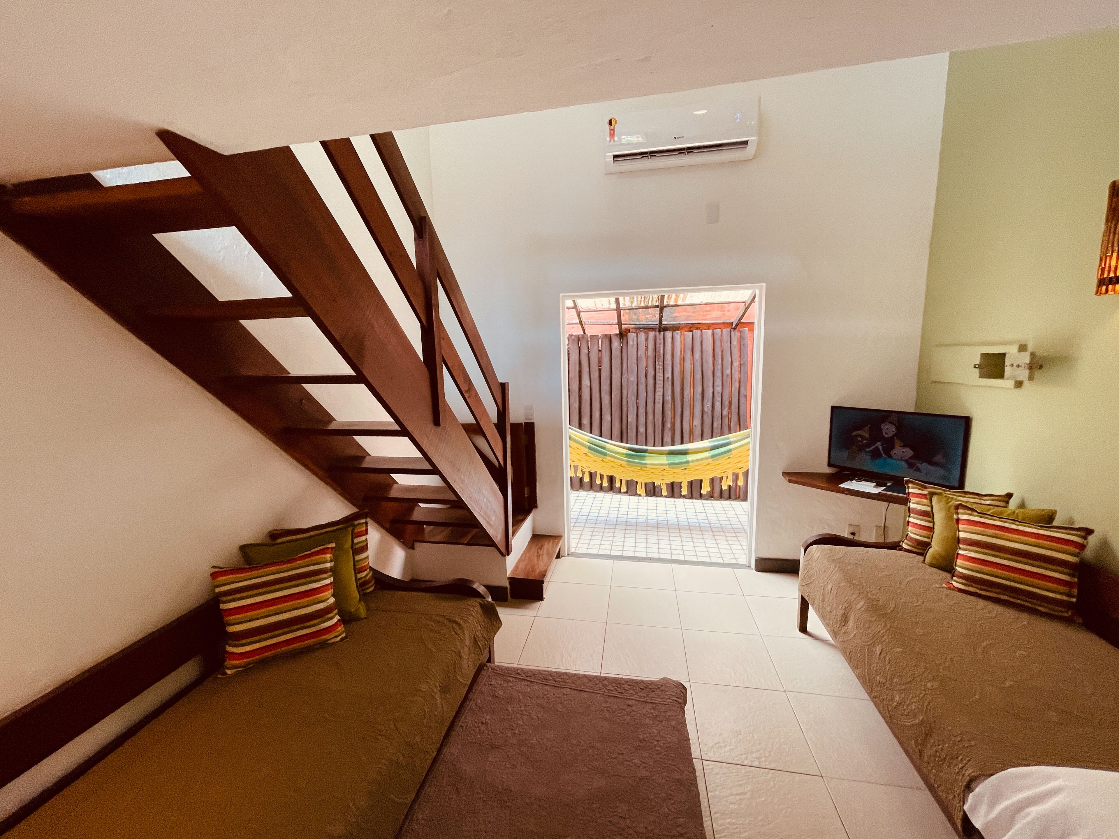 Una sala de estar con una escalera, un televisor y una hamaca.