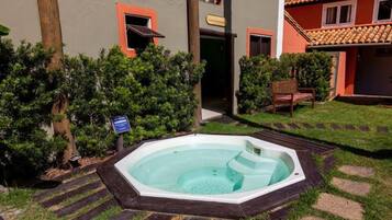 Uma banheira de hidromassagem em um jardim ajardinado com deck de madeira, cercada por vegetação e um edifício com paredes laranja e cinzas.