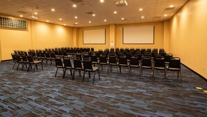 A conference room with rows of chairs, two large projection screens, and a carpeted floor. - Winners Inn Casino (Winnemucca)