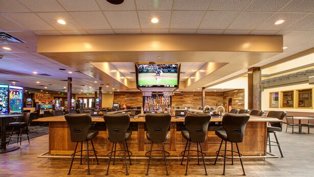 A bar area with a television screen, multiple bar stools, and a wooden counter. - Winners Inn Casino (Winnemucca)