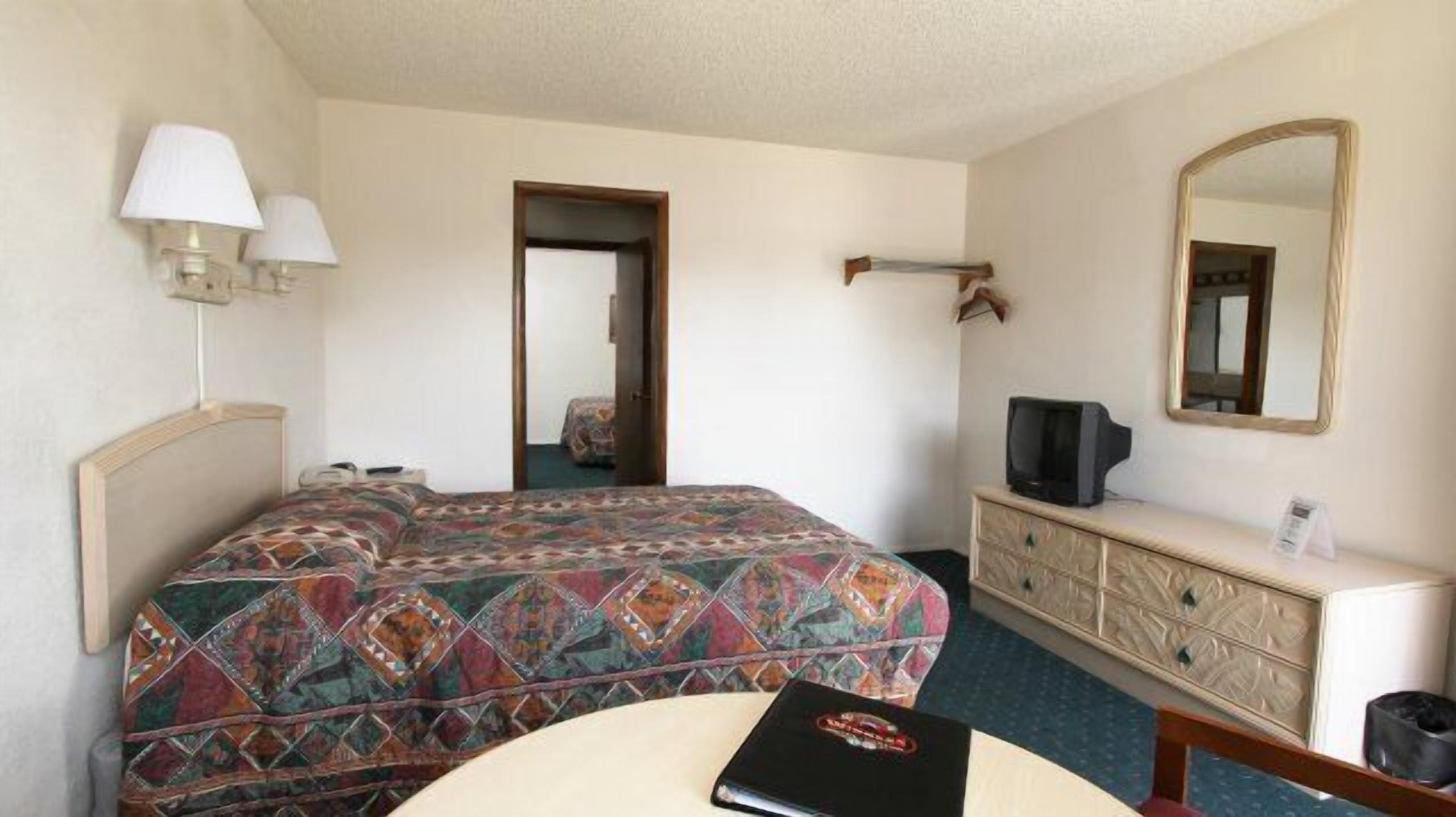 Ein Hotelzimmer mit Bett, Kommode, Fernseher und Spiegel.