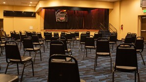 A conference room with rows of chairs, a stage with a banner, and a carpeted floor. - Winners Inn Casino (Winnemucca)