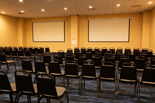 A conference room with rows of black chairs, two large projection screens, and carpeted flooring.
