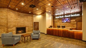 A lobby with a fireplace, two armchairs, a wooden reception desk, and a TV screen displaying 'Hotel Desk - Guest Services'. - Winners Inn Casino (Winnemucca)
