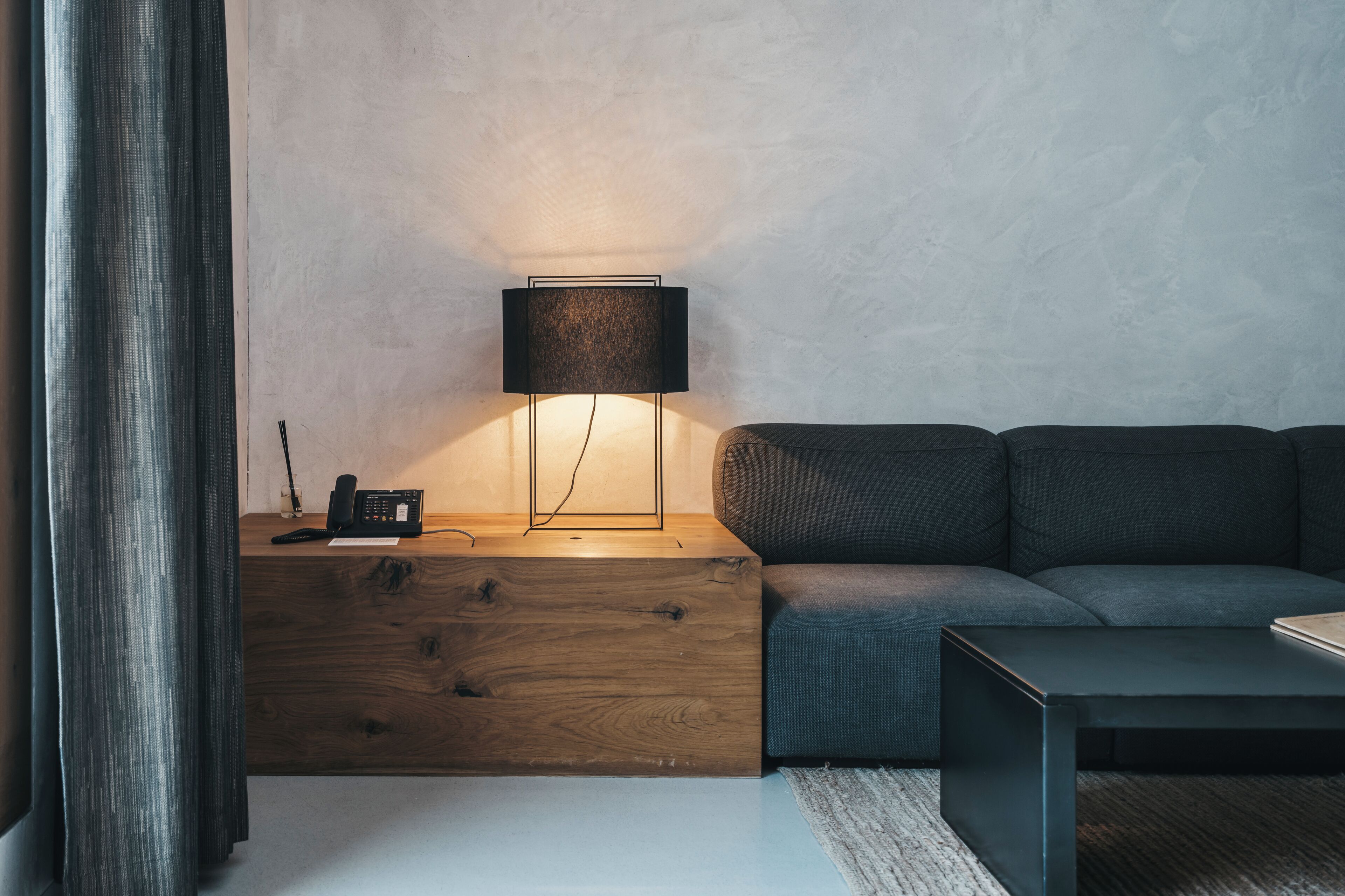 A modern living room with a wooden nightstand, a lamp, a sofa, and a coffee table.