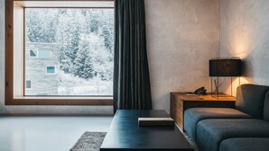 A modern living room with a large window, a dark sofa, a coffee table, and a lamp.