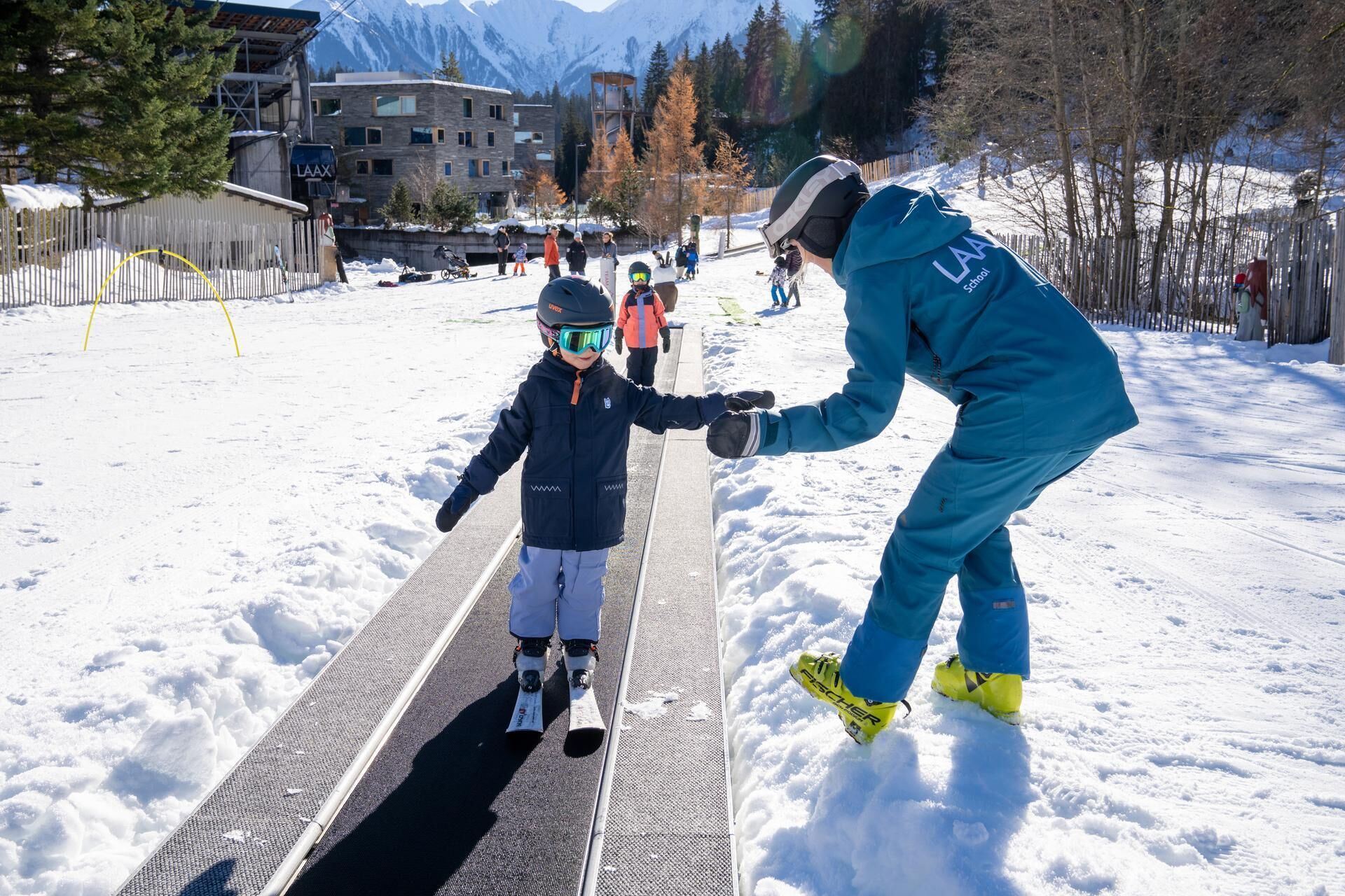 Pista de esquí con una persona ayudando a un niño a esquiar.