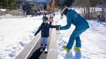 Pista de esquí con una persona ayudando a un niño a esquiar.
