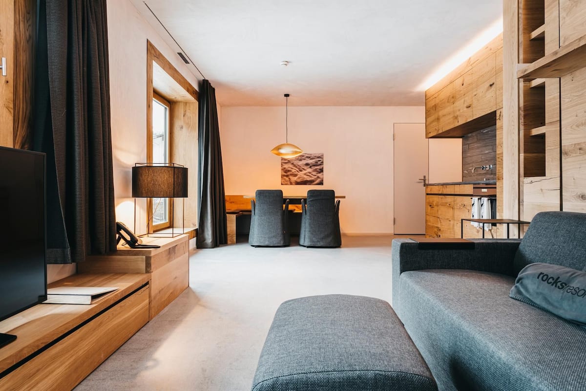 A modern living room with a sofa, a TV, and a dining area with chairs and a table.