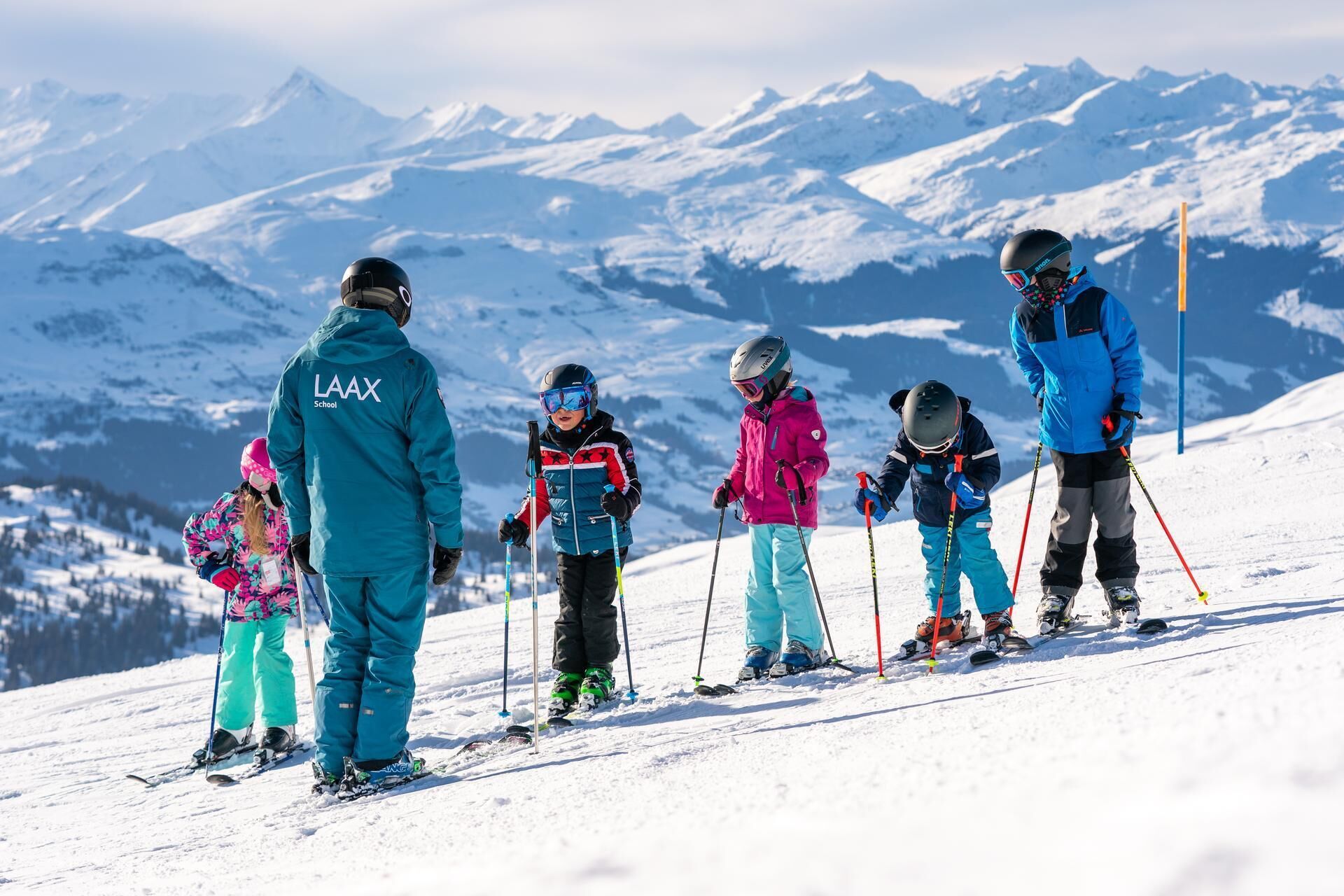 Eine Gruppe von Skifahrern auf einem verschneiten Hang, mit Bergen im Hintergrund.