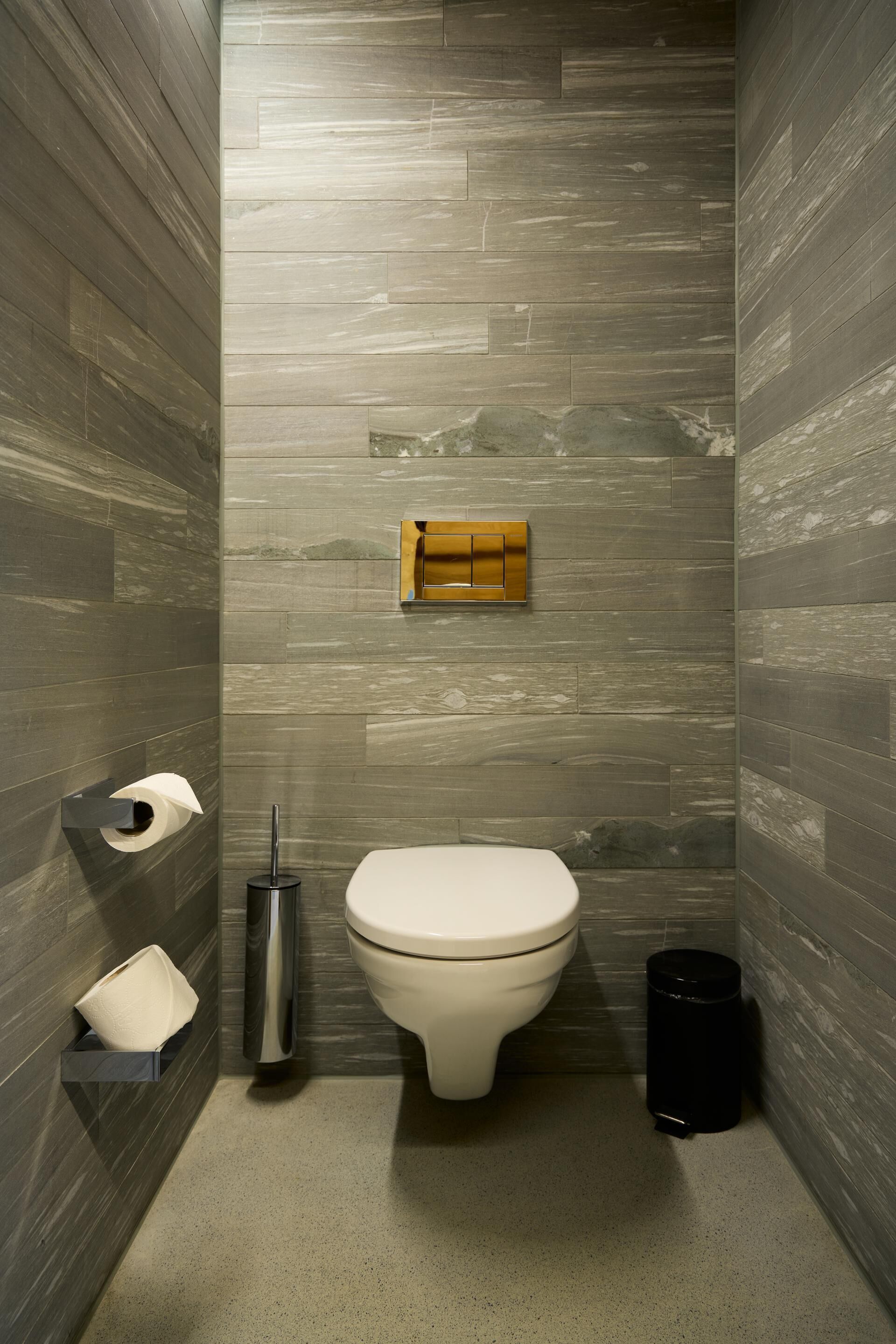 A modern bathroom with a toilet, a hand dryer, a trash bin, and a toilet paper holder on the wall.