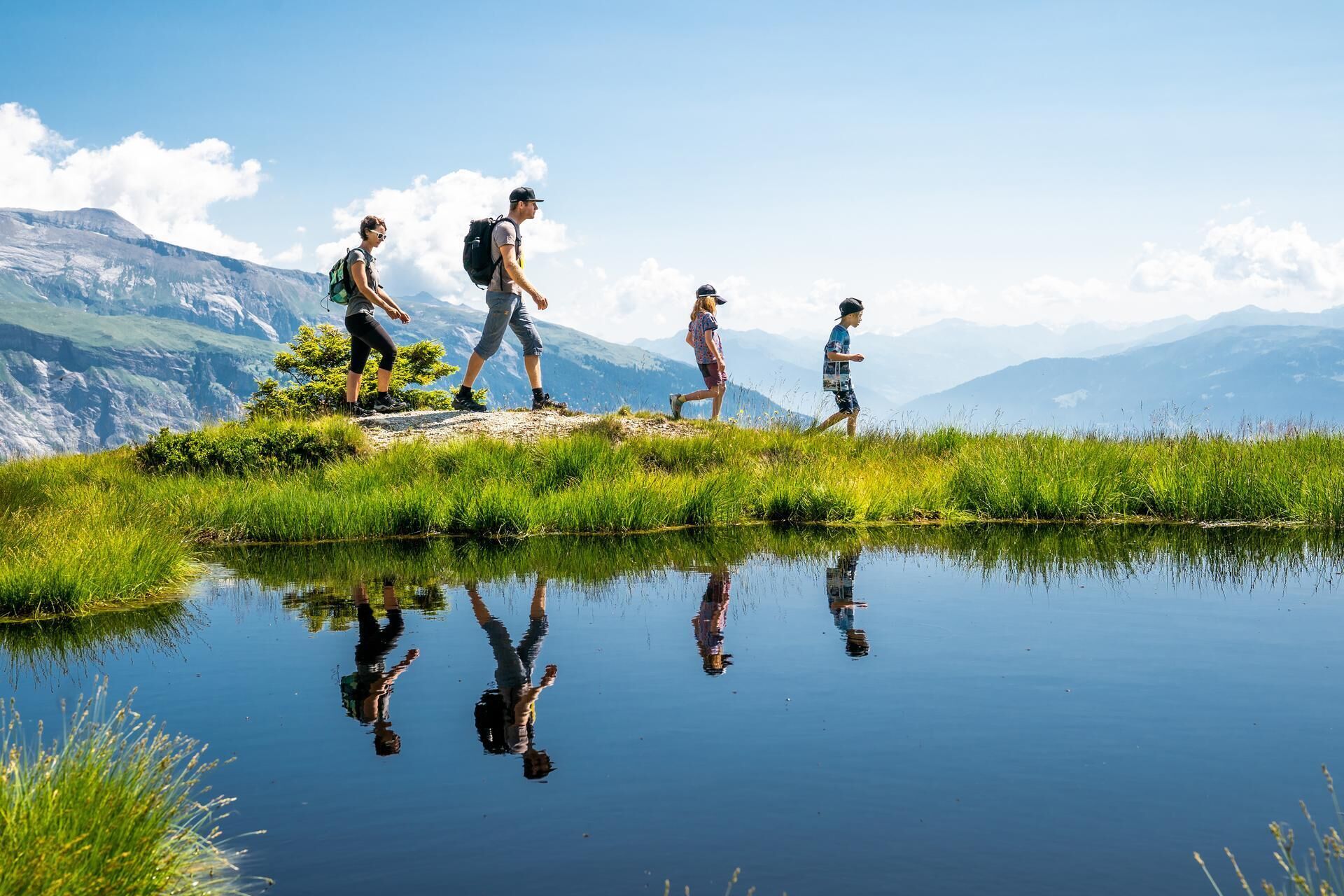A group of people hiking near a calm lake with mountains in the background.