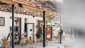 An outdoor cafe with wooden tables and chairs, hanging flower baskets, and a sign for 'FONDUE AUTOMAT'.