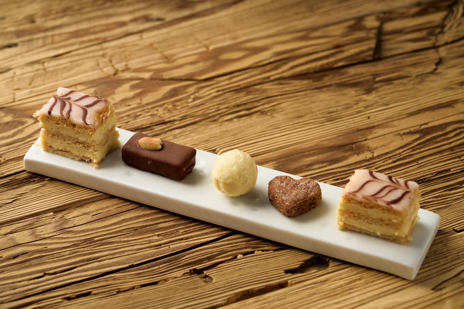 A white rectangular plate with five different desserts on a wooden table.