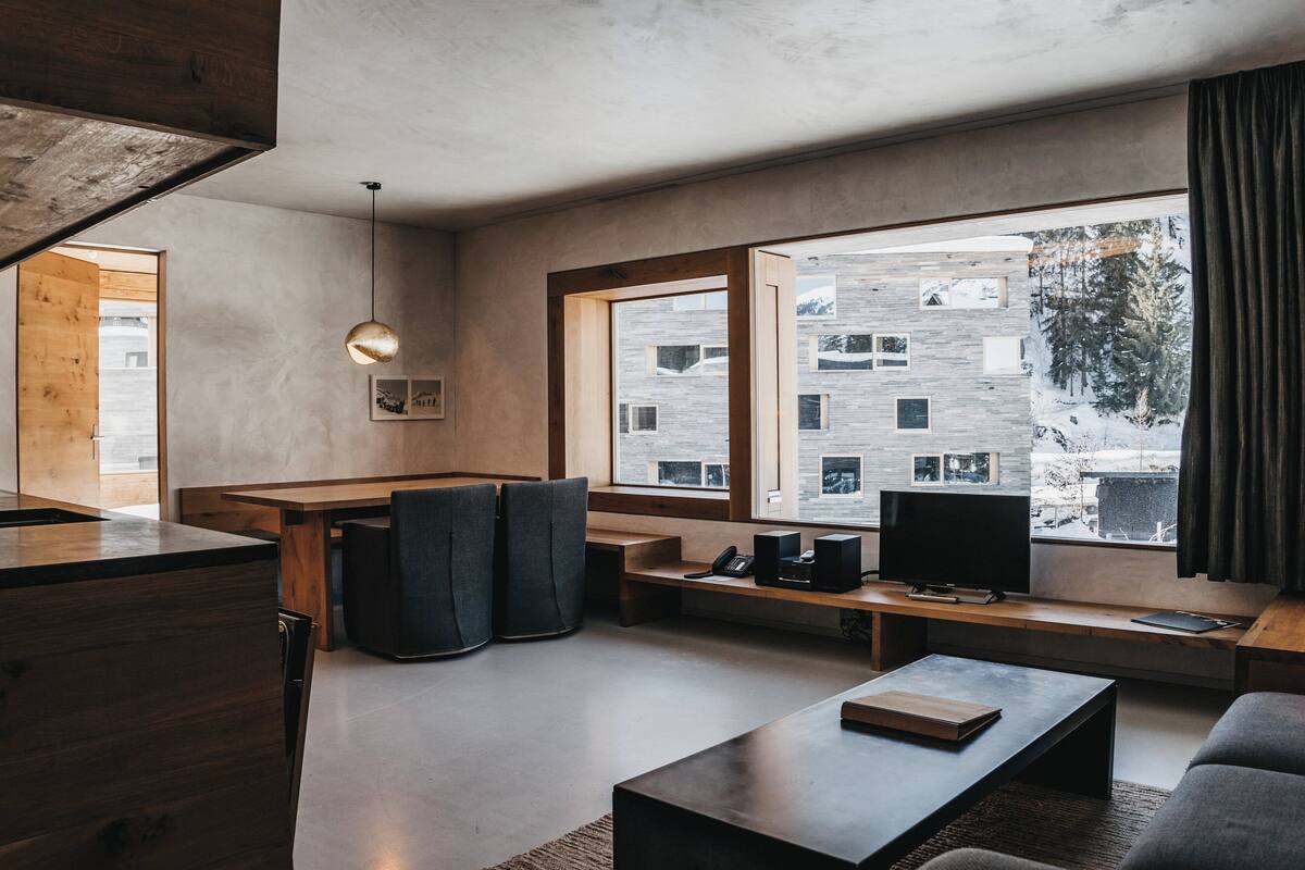 A modern living room with a large window, a wooden bench, a sofa, and a coffee table.