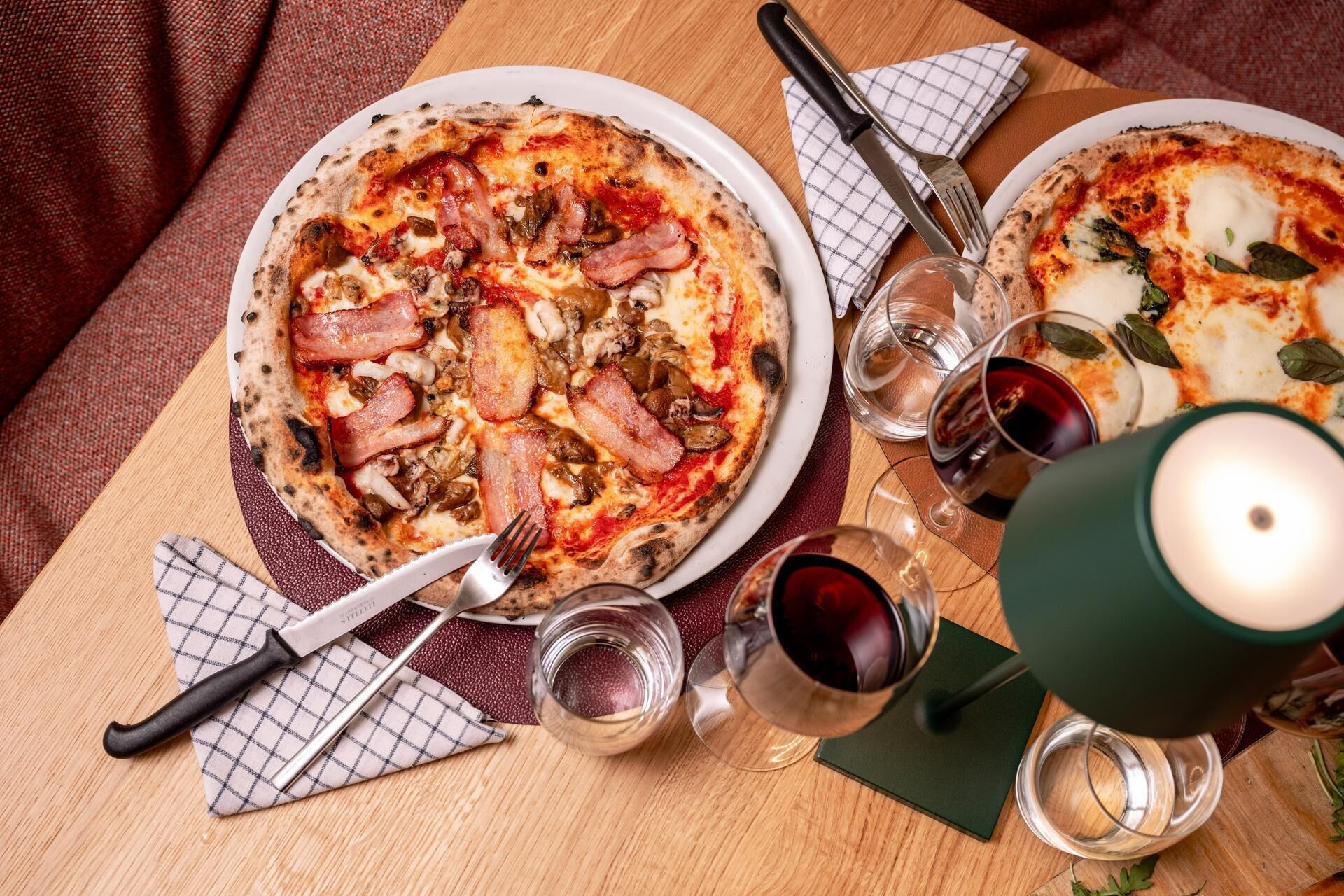 Dues pizzes als plats amb forques i gots de vi negre sobre una taula de fusta.