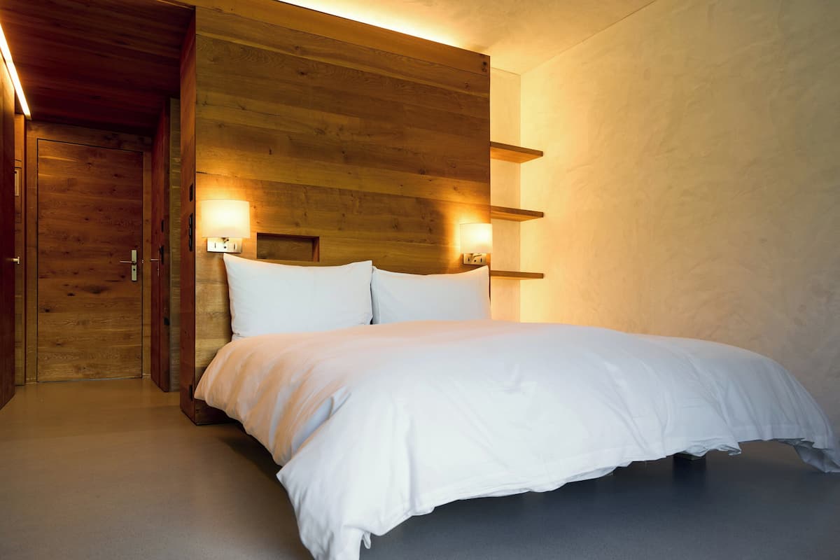 A bedroom with a wooden headboard, a bed with white bedding, and two wall-mounted bedside lamps.
