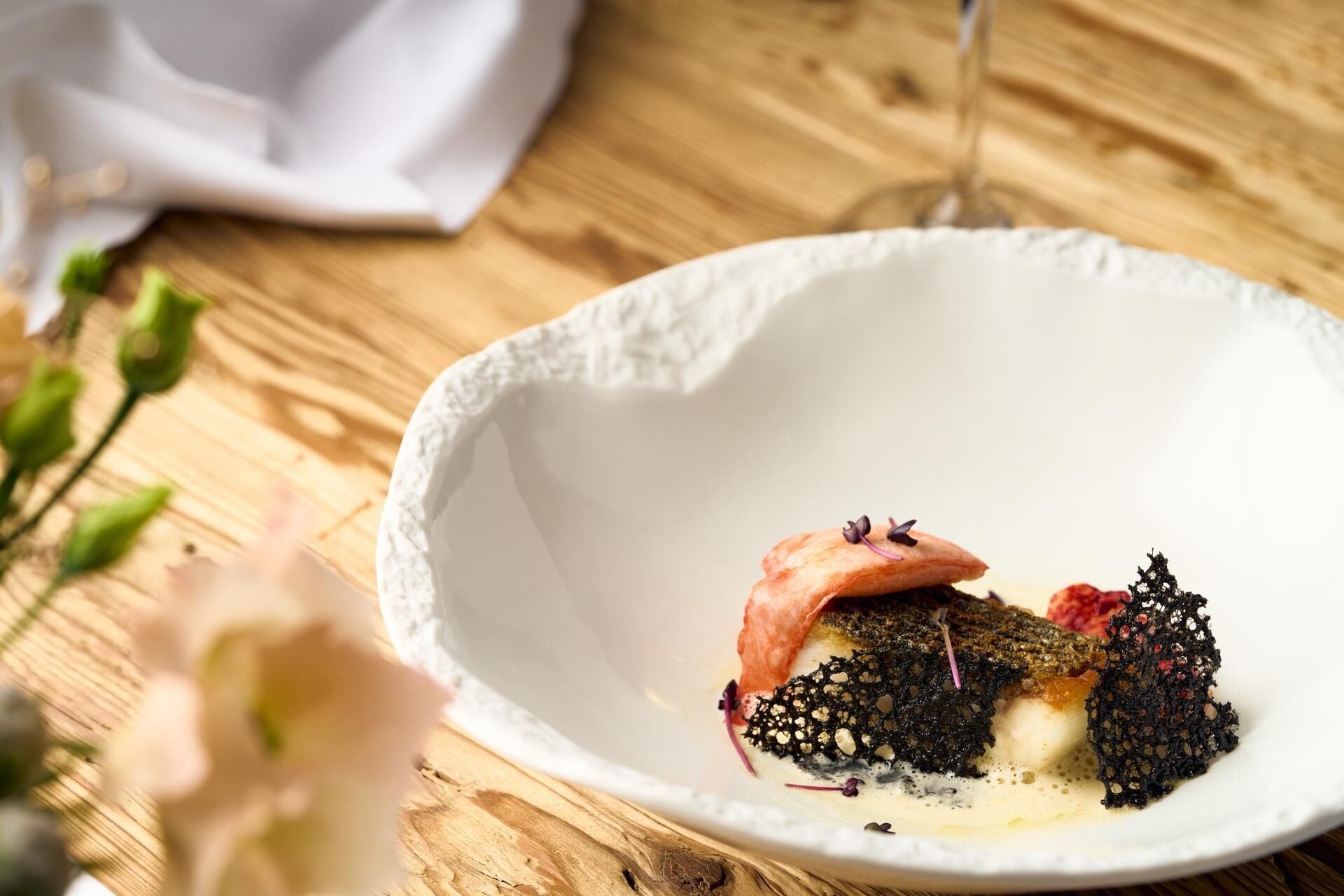 A white ceramic bowl on a wooden table with a glass of wine and a white napkin in the background.