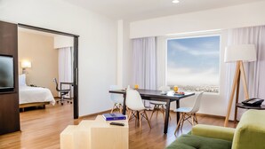 A hotel room with a bed, a desk with a chair, a green sofa, a TV, and a window with a view. - Fiesta Inn Queretaro Centro Sur (Querétaro)