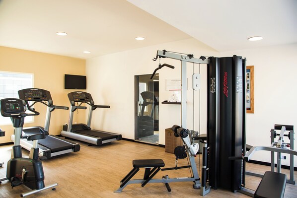 Un gimnasio con cintas de correr, elíptica, banco y estructura para sentadillas.