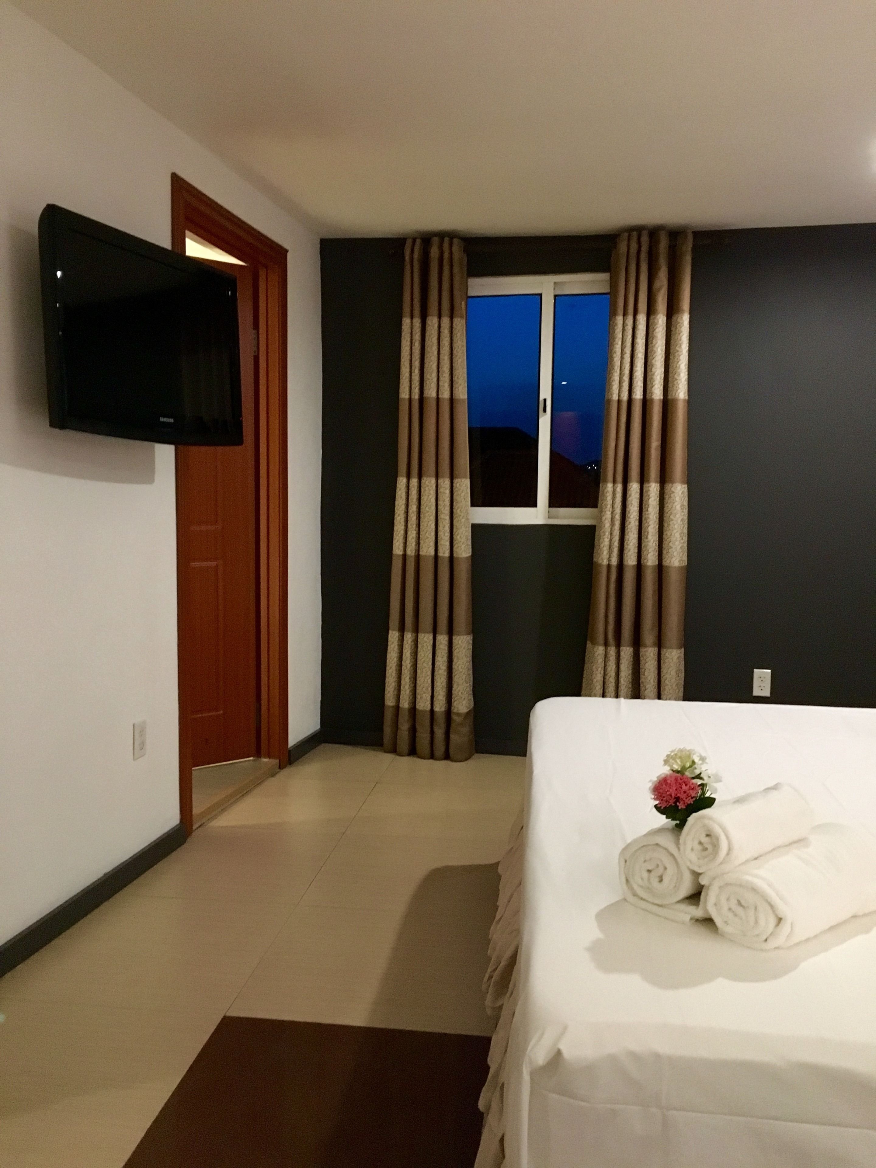 A hotel room with a bed, a TV mounted on the wall, and curtains on the window.