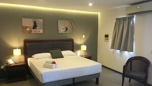 Una cama bien hecha con almohadas, una lámpara de noche, una silla y una obra de arte en la pared.