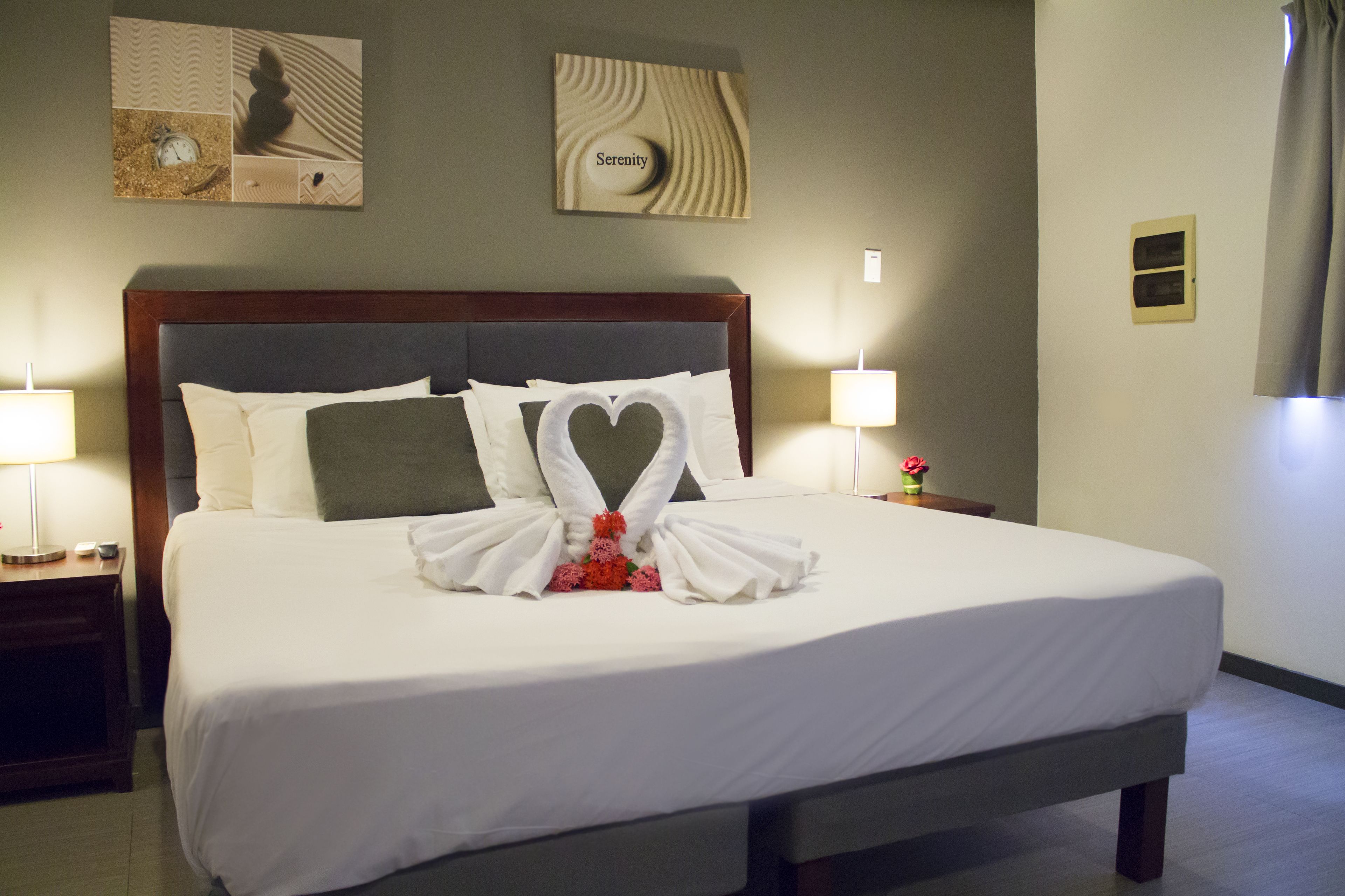 Un letto rifatto con lenzuola bianche e cuscini a forma di cuore, una testiera in legno e due abat-jour.
