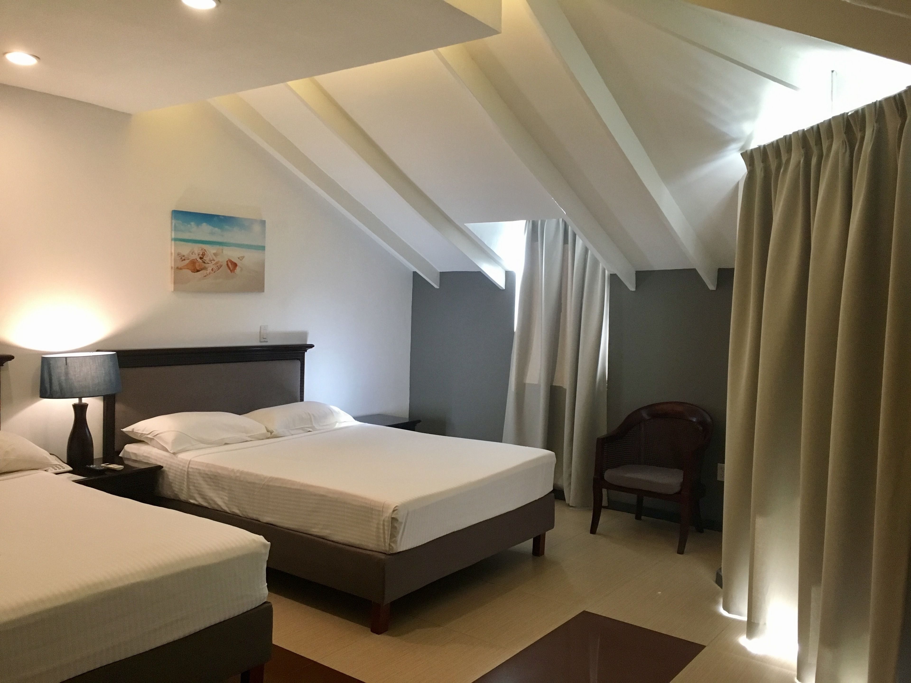 A hotel room with a large bed, a chair, a desk, and a painting on the wall.