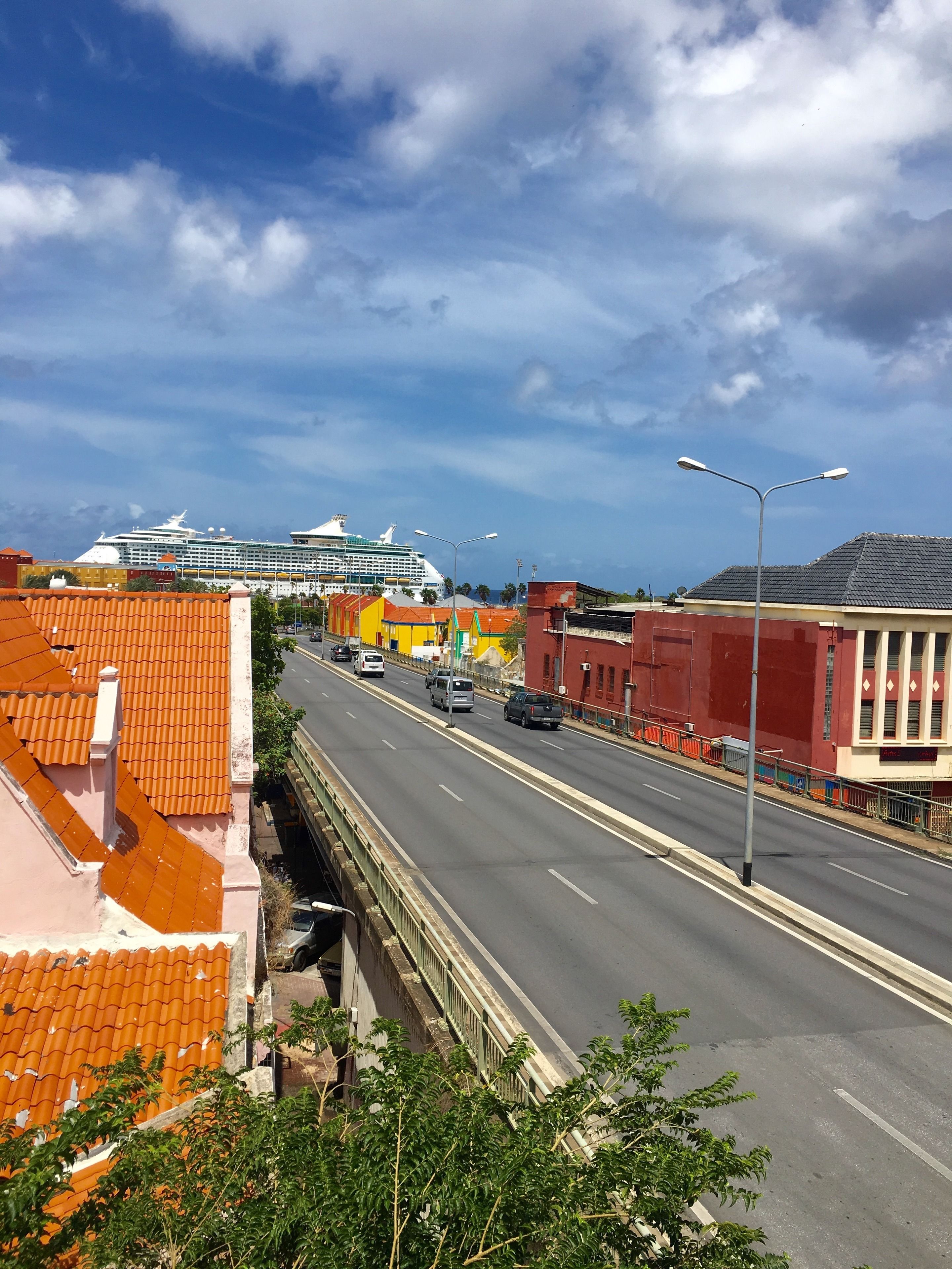 Una calle urbana con un crucero al fondo, edificios con fachadas naranja y amarilla, y cielo despejado.