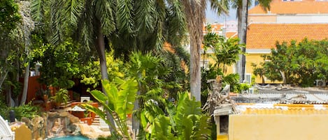 Zona de piscina con escalones que bajan hacia una fuente rodeada de palmeras y plantas tropicales.