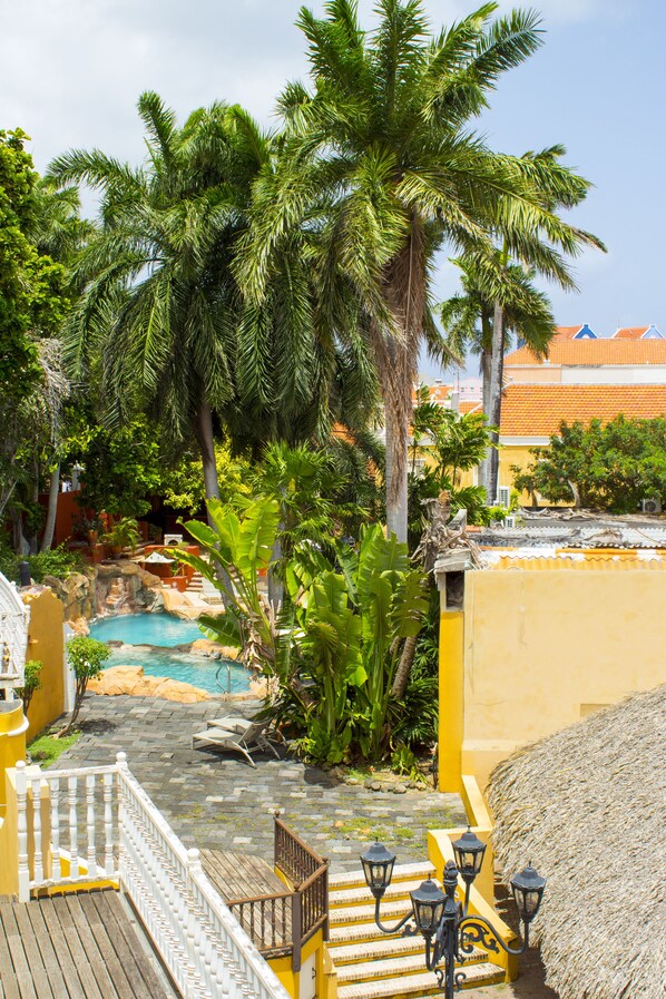 A pool area with steps leading down to a water feature surrounded by palm trees and tropical plants. - Curacao Suites Hotel (Willemstad)