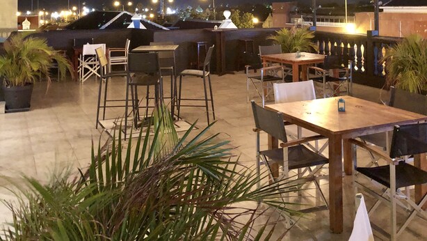Un patio al aire libre con mesas, sillas, luces colgantes y plantas en macetas.