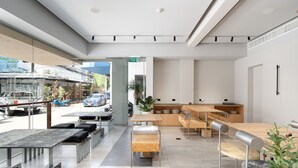 Un restaurant moderne au décor épuré et minimaliste, proposant différents types de sièges, notamment des tables et des bancs, et doté d’un espace extérieur visible donnant sur la rue.