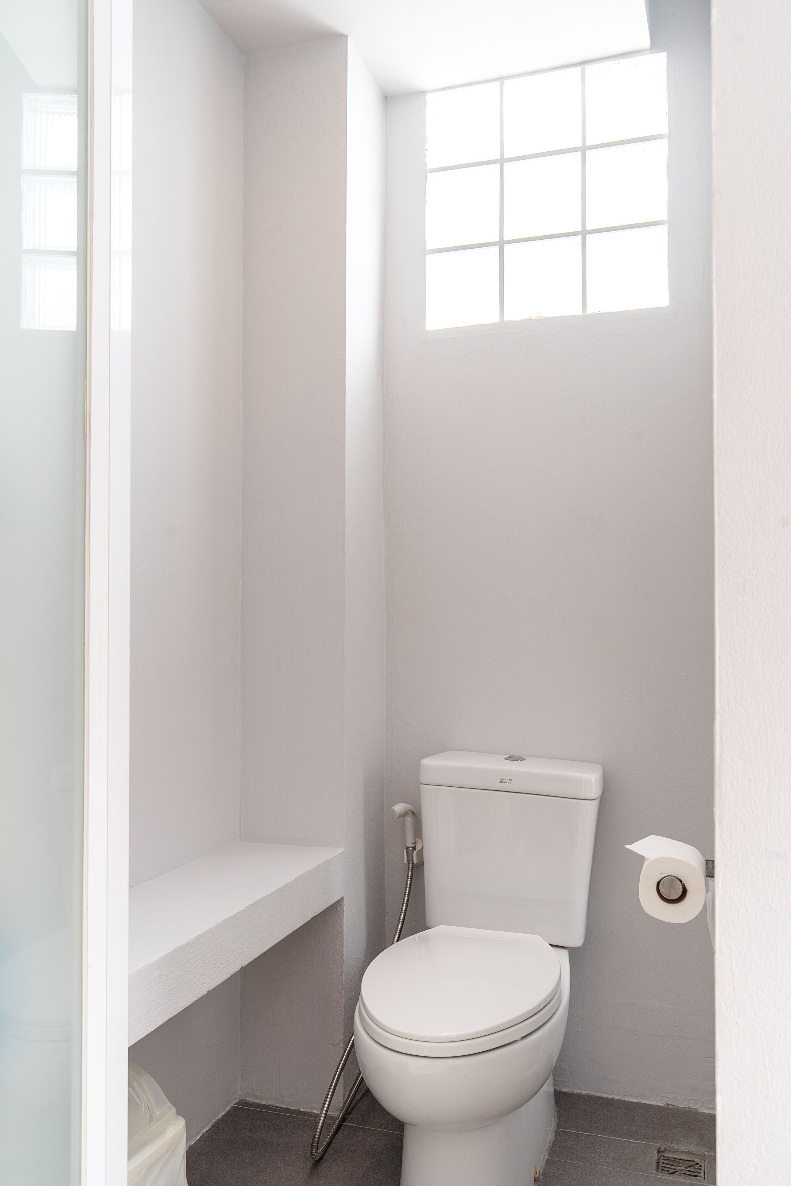A small, white bathroom with a toilet, a shower, and a window.