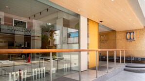 Un hall d’hôtel moderne avec une rambarde en verre, un comptoir d’accueil et une enseigne indiquant le Metz Pratunam Hotel.