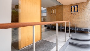 Un espace d’accueil moderne, avec un comptoir en bois, une cloison en verre et une enseigne indiquant le « Metz Pratunam Hotel ».