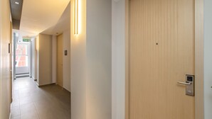 Un couloir avec une porte en bois sur la droite, un luminaire sur la gauche et un panneau indiquant la sortie.