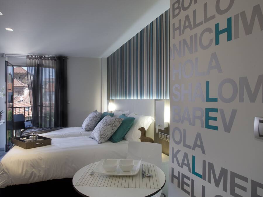 Habitación de hotel moderna con cama, mesita de noche y vistas a la ciudad.