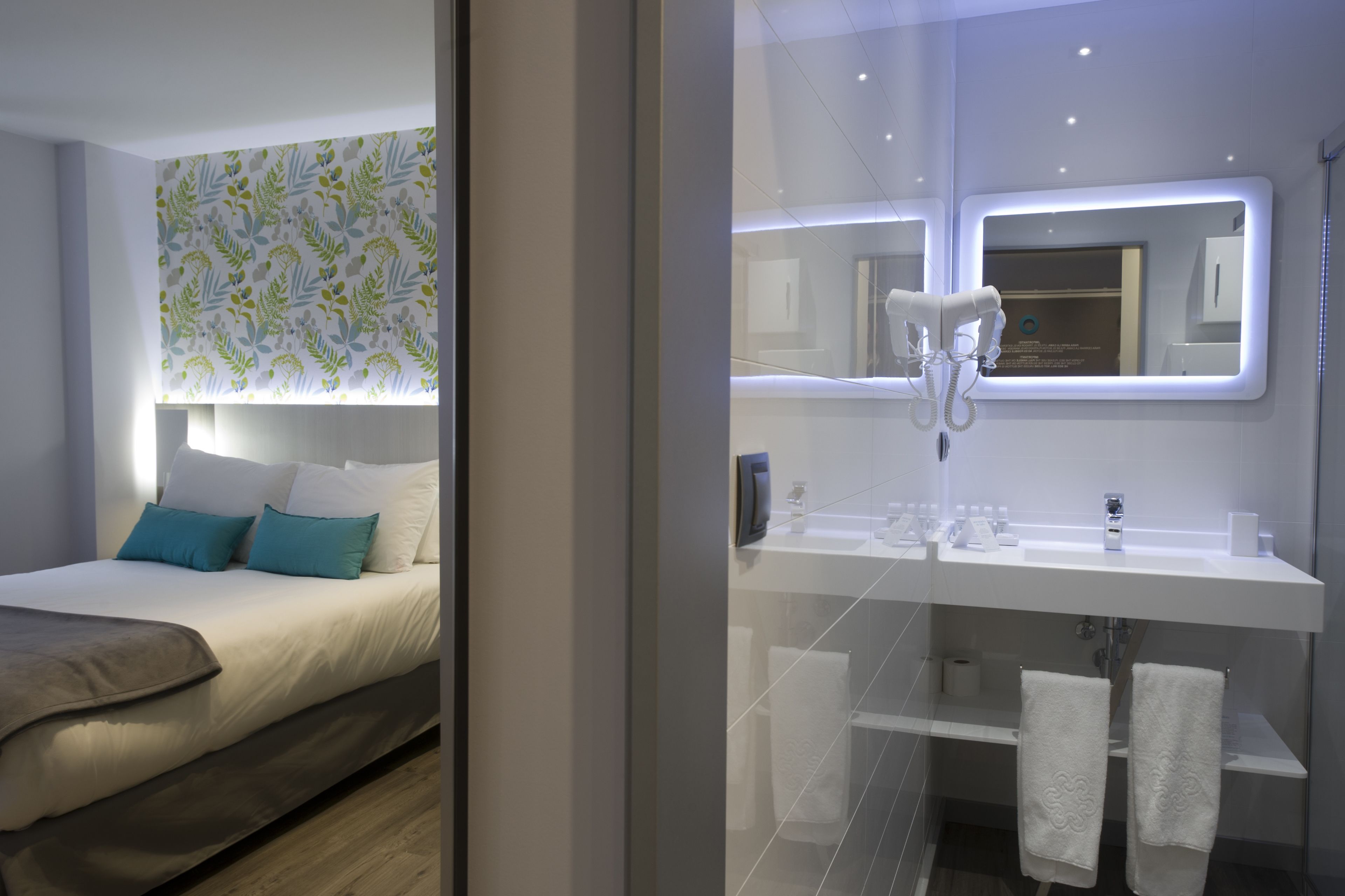 Una habitación de hotel moderna con una cama bien hecha, un espejo grande sobre el lavabo y una zona de ducha.