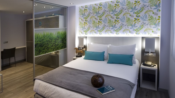 Een moderne hotelkamer met een groot bed, een bureau en uitzicht op groen via een glazen deur.