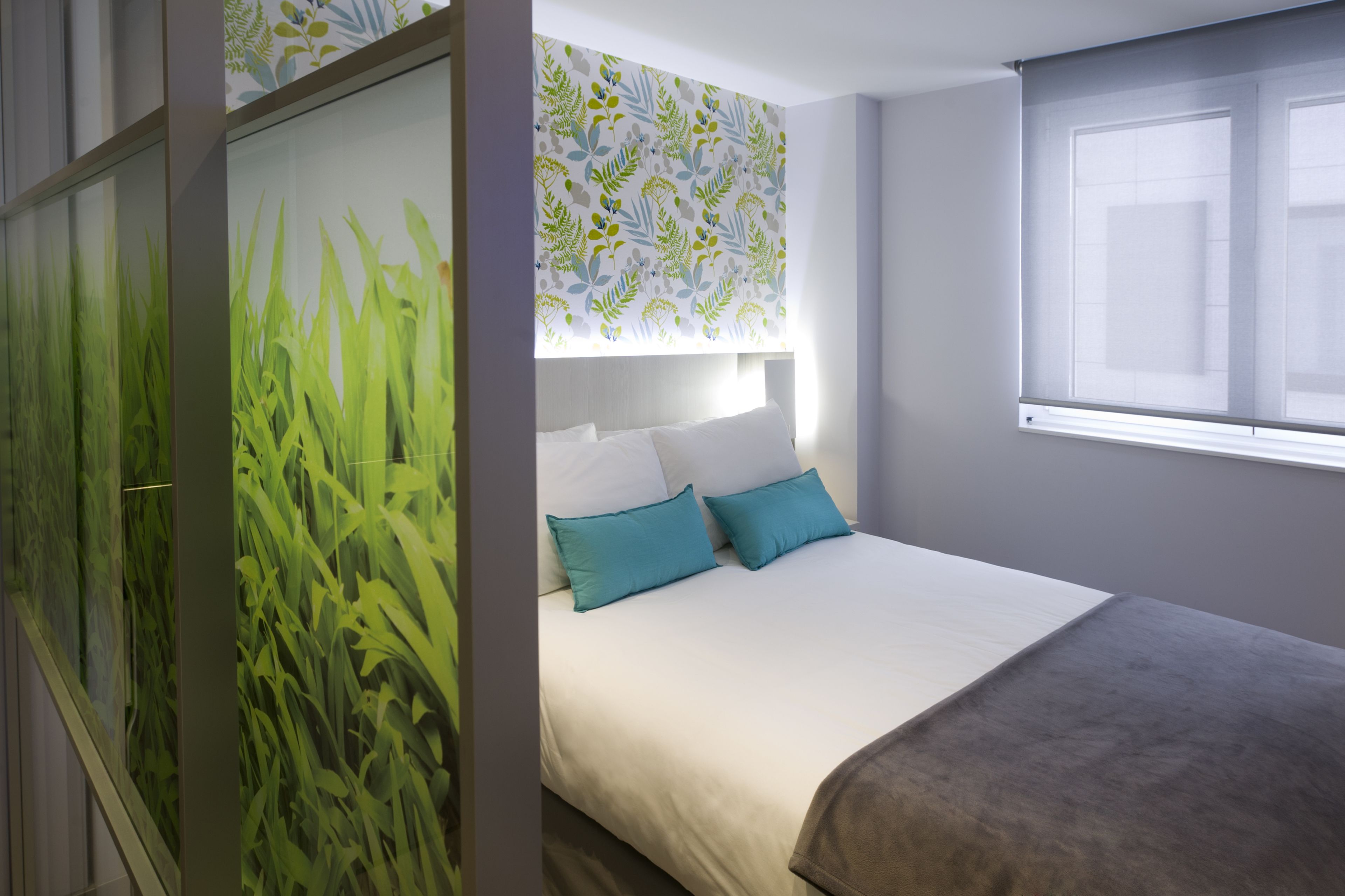 Un dormitorio con cama, ventana y pared decorada con un diseño de hojas.