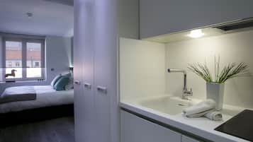 Un dormitorio moderno con cama, mesita de noche, ventana y baño con lavabo y espejo.