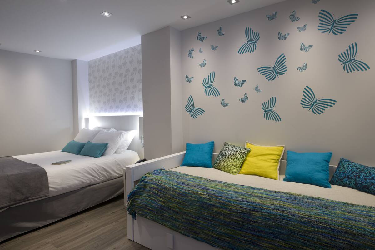 Een moderne slaapkamer met twee bedden, elk met kussens in verschillende kleuren en een bedsprei met dessin.
