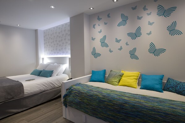 Un dormitorio moderno con dos camas, cada una con almohadones de colores distintos y un edredón estampado.