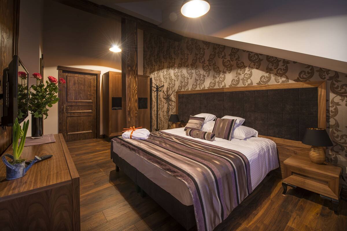 A bedroom with a large bed, wooden wardrobe, and a mirror.