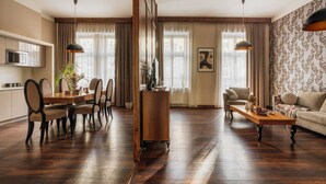 A spacious living room with a wooden floor, a dining area with a wooden table and chairs, a sofa, and a coffee table. - Topolowa Residence by StayLab (Kraków)