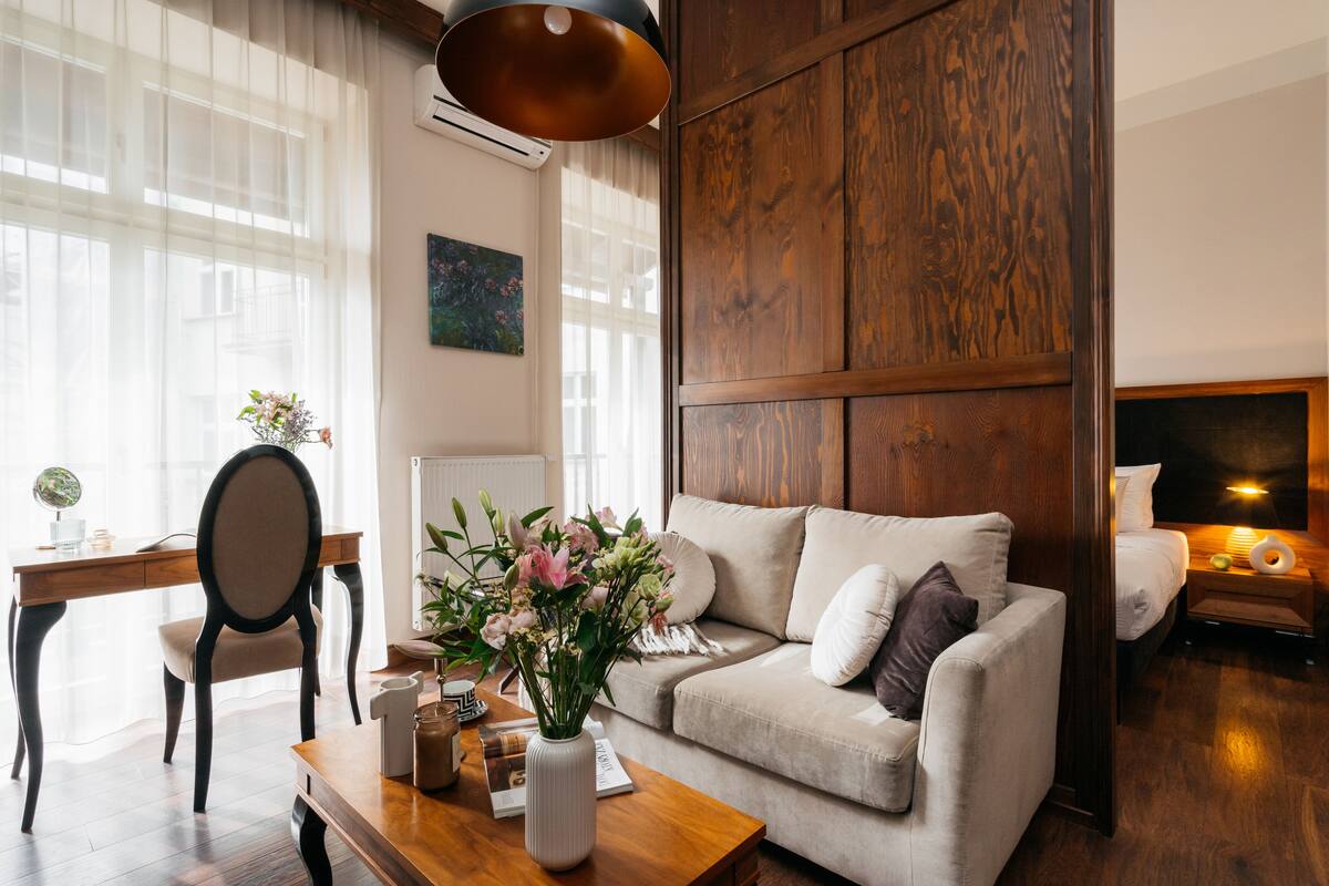 A cozy living room with a wooden panel wall, a sofa, a coffee table with a vase of flowers, a desk with a chair, and a globe.
