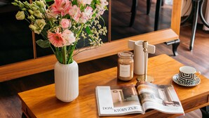 A wooden coffee table with a vase of flowers, a candle, a magazine, and a cup. - Topolowa Residence by StayLab (Kraków)